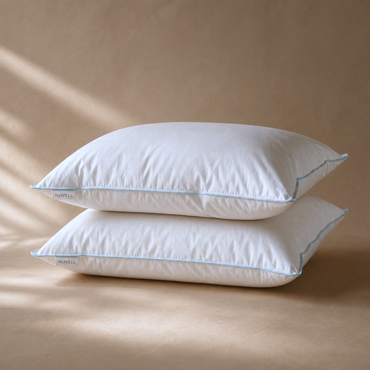 Two white NUVELL Firm pillows with blue piping on a warm neutral surface