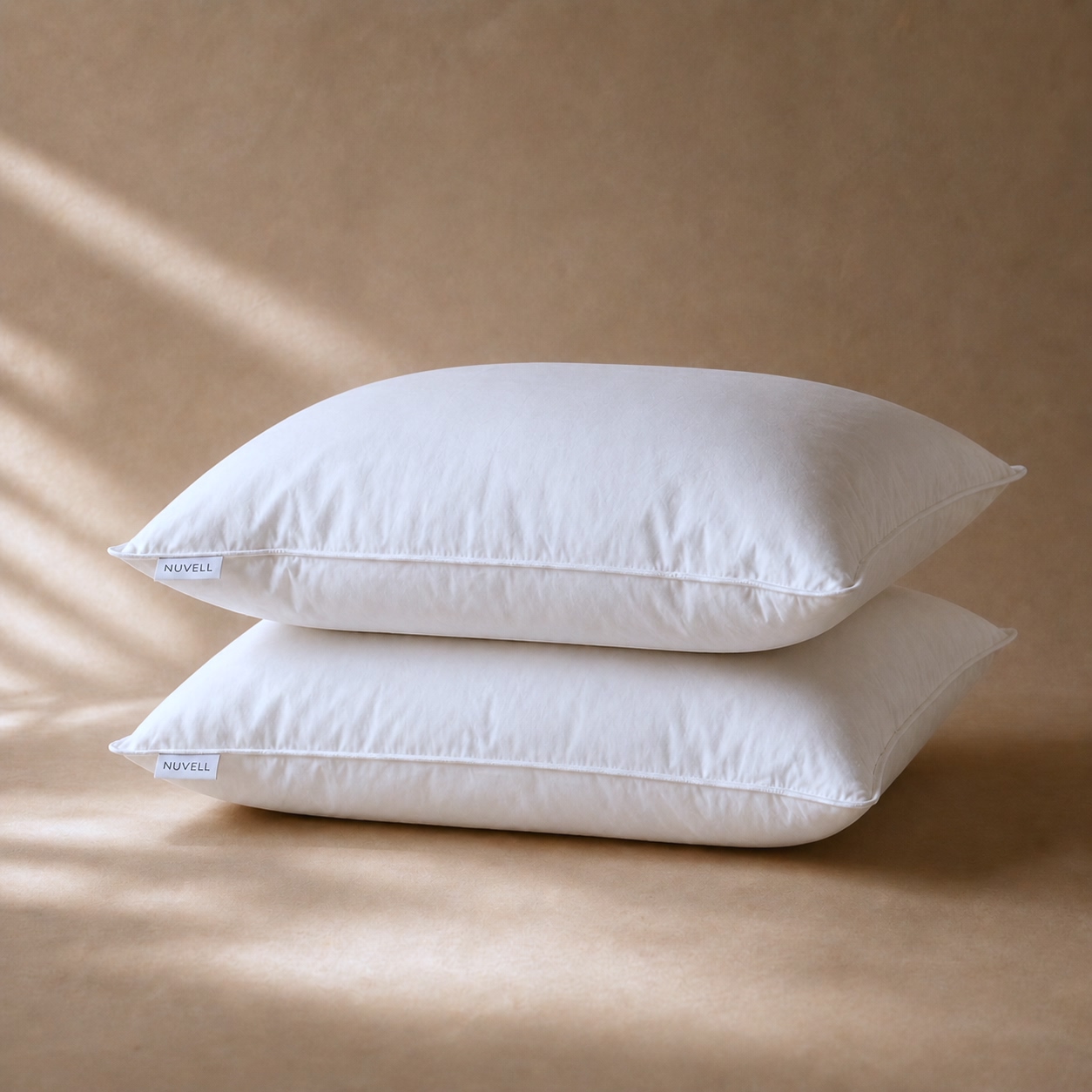 Two white NUVELL soft pillows on a warm neutral surface