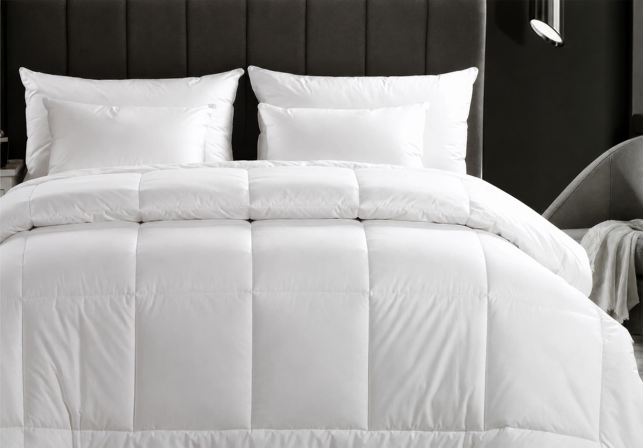 White quilt and pillows in a dark hotel-style bedroom